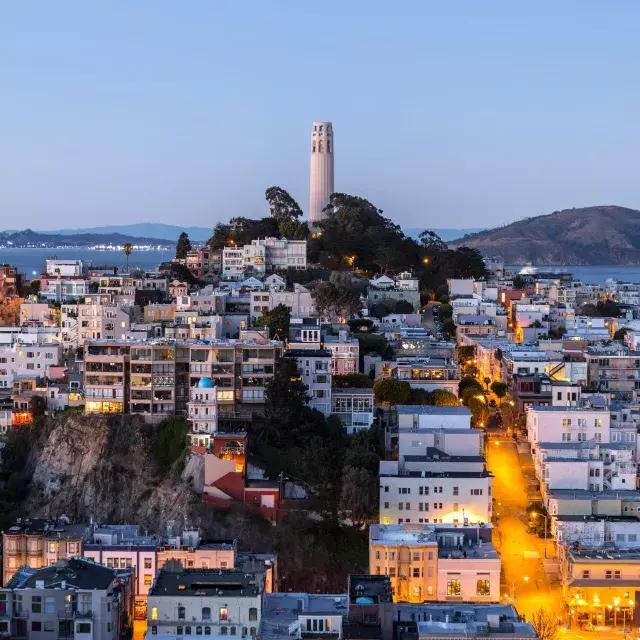 Der Coit Tower von San Francisco in der Abenddämmerung, 前面是灯火通明的街道，后面是贝博体彩app湾。.